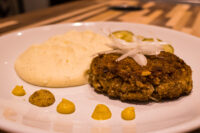 Karbenátky (Czech Burger) Karbenátky (Czech Burger) patty topped with sliced onion, served with mashed potato, mustard dots, and pickles.