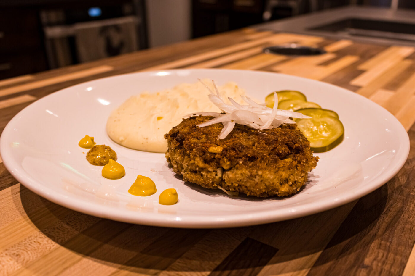 Karbenátky (Czech Burger) Karbenátky (Czech Burger) patty on a white plate with mashed potato, pickles, and mustard.