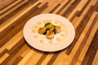 Scallops with Spicy Sauce Plate of Scallops with Spicy Sauce, seared scallops on greens with a lemon wedge and yellow sauce dots.