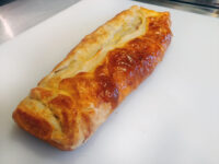 Apple Strudel Baked Apple Strudel loaf with braided, golden puff pastry crust on a white cutting board.