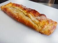 Apple Strudel Golden baked Apple Strudel dusted with powdered sugar on a white cutting board.