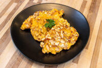 Almond Chicken Schnitzel Almond Chicken Schnitzel with a sliced almond crust and parsley garnish on a black plate.