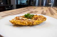 Almond Chicken Schnitzel Almond Chicken Schnitzel cutlet coated in sliced almonds, garnished with parsley on a white plate.