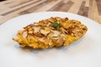 Almond Chicken Schnitzel on a white plate, coated in sliced almonds and garnished with parsley.