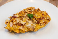 Almond Chicken Schnitzel Golden Almond Chicken Schnitzel crusted with sliced almonds, garnished with parsley on a white plate.