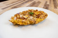 Almond Chicken Schnitzel Golden Almond Chicken Schnitzel coated in sliced almonds, garnished with herb, on a white plate.