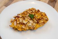 Almond Chicken Schnitzel Almond Chicken Schnitzel coated in sliced almonds, garnished with parsley on a white plate.