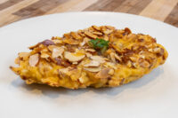 Almond Chicken Schnitzel on a white plate, coated in sliced almonds with a parsley garnish