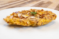 Almond Chicken Schnitzel fillet coated in sliced almonds on a white plate, garnished with herb.