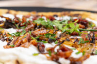 Lokše Flat Bread with Bryndza Cheese Substitute and Bacon Close-up of Lokše Flat Bread with Bryndza Cheese Substitute and Bacon, showing cheese, onions, bacon, and herbs.