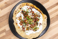 Lokše Flat Bread with Bryndza Cheese Substitute and Bacon Lokše Flat Bread with Bryndza Cheese Substitute and Bacon topped with white sauce, bacon, onion bits, and chives.