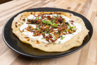 Lokše Flat Bread with Bryndza Cheese Substitute and Bacon Lokše Flat Bread with Bryndza Cheese Substitute and Bacon on a black plate, topped with crispy bacon and chives.