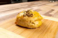 A single golden Pagáče (Pagache) with Cracklings bun topped with caraway seeds on a wooden board.