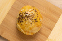 Single golden Pagáče (Pagache) with Cracklings bun topped with caraway seeds and salt on a wooden board.