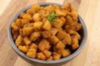 Bowl of golden-brown diced Pork Cracklings (Škvarky) & Lard (Sádlo), garnished with parsley, on a wood surface.
