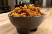 Bowl of golden-brown Pork Cracklings (Škvarky) with a green garnish leaf on a wooden table.