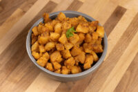 Gray bowl of golden-brown Pork Cracklings (Škvarky), garnished with green herb, on a wooden table.