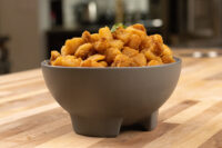Bowl of golden-brown Pork Cracklings (Škvarky) topped with a green herb sprig on a wooden counter.