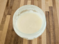 Glass jar of pale, creamy rendered lard (Sádlo) from Pork Cracklings recipe on a wooden surface.