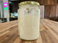 Jar of white solidified Sádlo (lard) from the Pork Cracklings (Škvarky) & Lard recipe on a wooden counter.