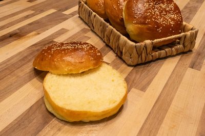 Burger Buns A split Burger Bun with sesame seeds in front of more buns piled in a woven basket on wood.