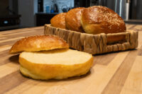 Burger Buns A sliced Burger Bun in front, golden crust with sesame seeds, more buns piled in a woven basket behind.