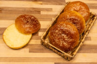 Burger Buns Four sesame-topped Burger Buns in a woven basket beside one sliced open on a wooden board