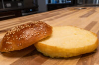 Burger Buns A sesame-seed Burger Bun halved, cut side up, on a wooden board.