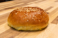 Burger Buns A golden, sesame-topped Burger Buns sits on a wooden countertop.