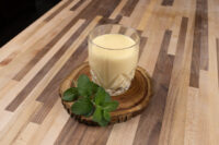 Czech Egg Liqueur – Czech Eggnog Glass of Czech Egg Liqueur – Czech Eggnog on a wood slice coaster with fresh mint on a striped wood table.