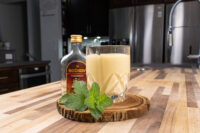 Czech Egg Liqueur – Czech Eggnog Glass of Czech Egg Liqueur – Czech Eggnog beside a Božkov Tuzemský bottle and fresh mint on a wood slice.