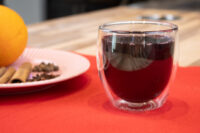 Double-walled glass of Czech Mulled Wine Svarak beside a plate of cinnamon sticks, cloves, and an orange.