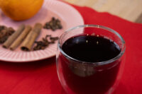 Glass of Czech Mulled Wine Svarak beside a plate with cinnamon sticks, cloves, and an orange.