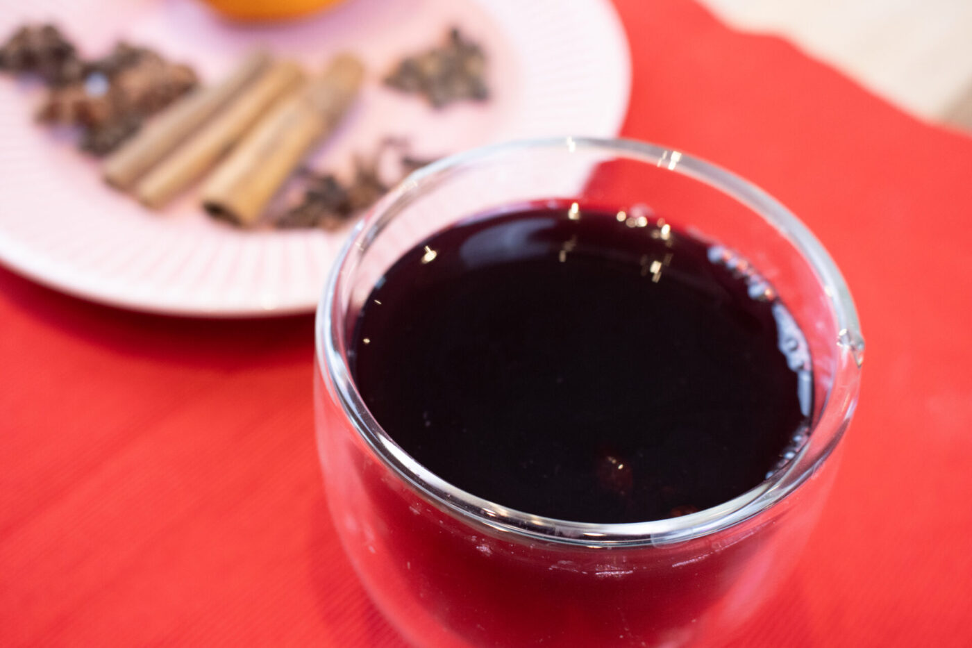 Czech Mulled Wine Svarak Glass of dark red Czech Mulled Wine Svarak on a red cloth, with cinnamon sticks and cloves on a plate behind it.