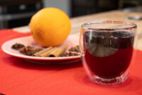 Glass of Czech Mulled Wine Svarak beside a plate of cinnamon, star anise, cloves, and an orange