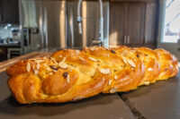 Braided Christmas Vánočka (Houska) loaf topped with sliced almonds on a dark wood counter.