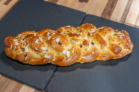 Braided Christmas Vánočka (Houska) loaf topped with sliced almonds on a dark slate board.