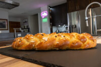 Braided Christmas Vánočka (Houska) loaf topped with sliced almonds, resting on a dark slate board.