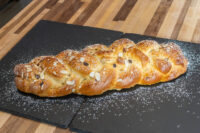 Braided Christmas Vánočka (Houska) loaf with almonds and raisins, dusted with powdered sugar on slate.