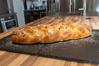 Braided Christmas Vánočka (Houska) loaf topped with sliced almonds and powdered sugar on a dark slate board.