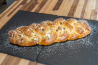 Braided Christmas Vánočka (Houska) topped with sliced almonds and powdered sugar on a slate board.