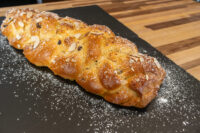 Braided Christmas Vánočka (Houska) topped with sliced almonds and powdered sugar on a dark slate board.