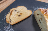 Sliced Christmas Vánočka (Houska) with raisins, dusted with powdered sugar on a slate board.