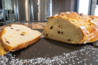 Braided Christmas Vánočka (Houska) loaf topped with almonds, with two raisin-studded slices cut beside it.