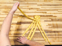 Hands braiding strands of yellow dough into a knotted bundle for Christmas Vánočka (Houska)