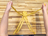 Hands shaping braided dough strands into a knotted star pattern for Christmas Vánočka (Houska).