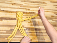 Hands braiding strands of raisin-studded dough for Christmas Vánočka (Houska) on a wooden countertop