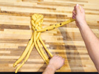 Hands braiding raisin-studded dough strands for Christmas Vánočka (Houska) on a wooden board.