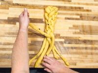 Hands braiding strands of yellow dough for Christmas Vánočka (Houska) on a wooden board