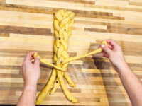 Hands shaping braided strands of yellow dough with raisins for Christmas Vánočka (Houska).